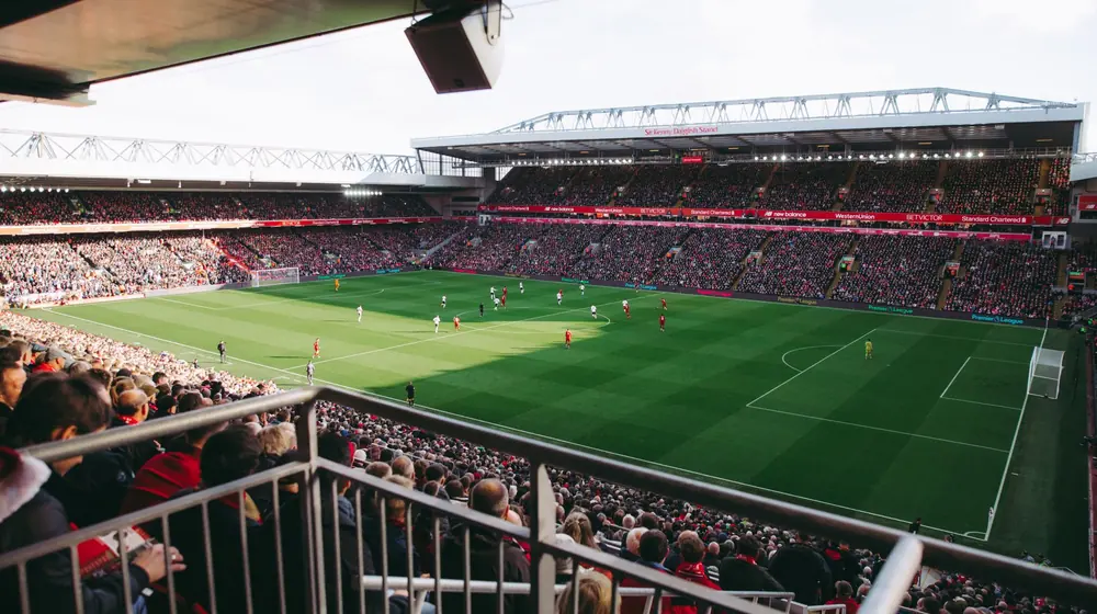 Vista da arquibancada de um estádio de futebol lotado durante uma partida, com o gramado ao fundo